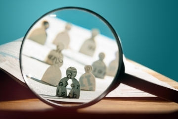 Magnifying glass focusing on paper cutouts of people